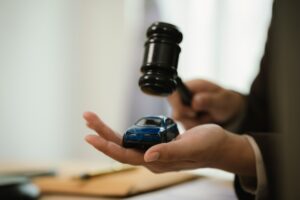 A person holds a small blue toy car in one hand and a judges gavel in the other, symbolizing car-related legal decisions or auction.