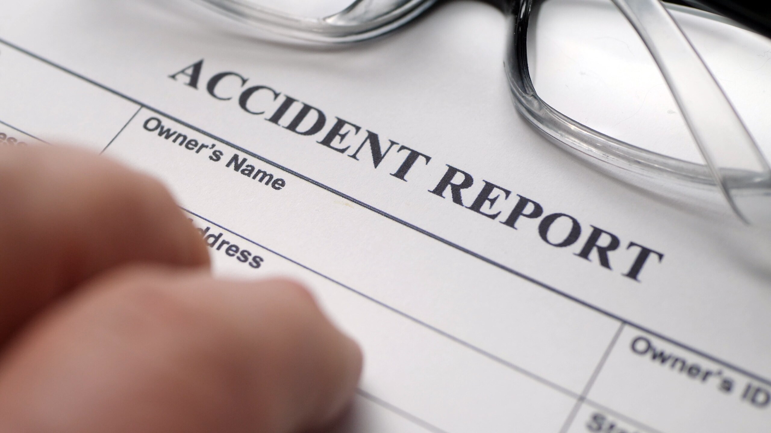 A hand reaching toward an accident report form with glasses resting at the top.